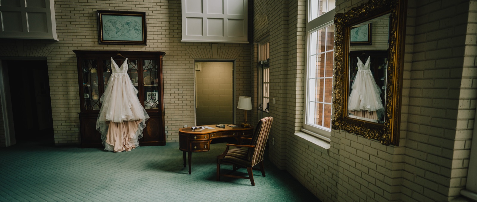 Wedding dress hanging in a vintage room, reflected in a gold mirror